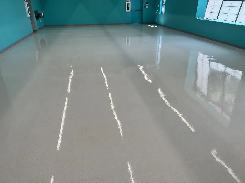 An empty hallway with a shiny floor reflecting overhead lighting, and turquoise walls with closed doors.