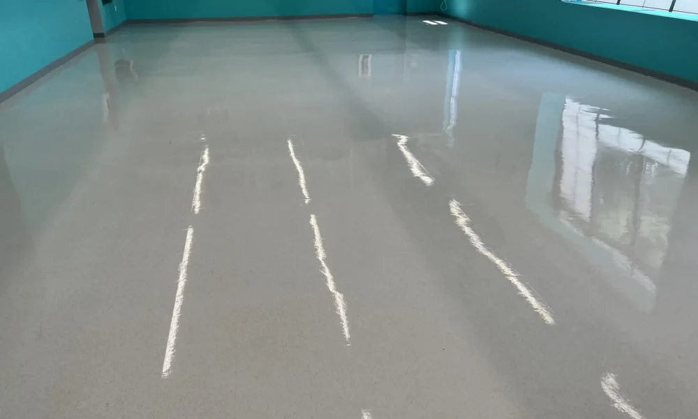 An empty hallway with a shiny floor reflecting overhead lighting, and turquoise walls with closed doors.